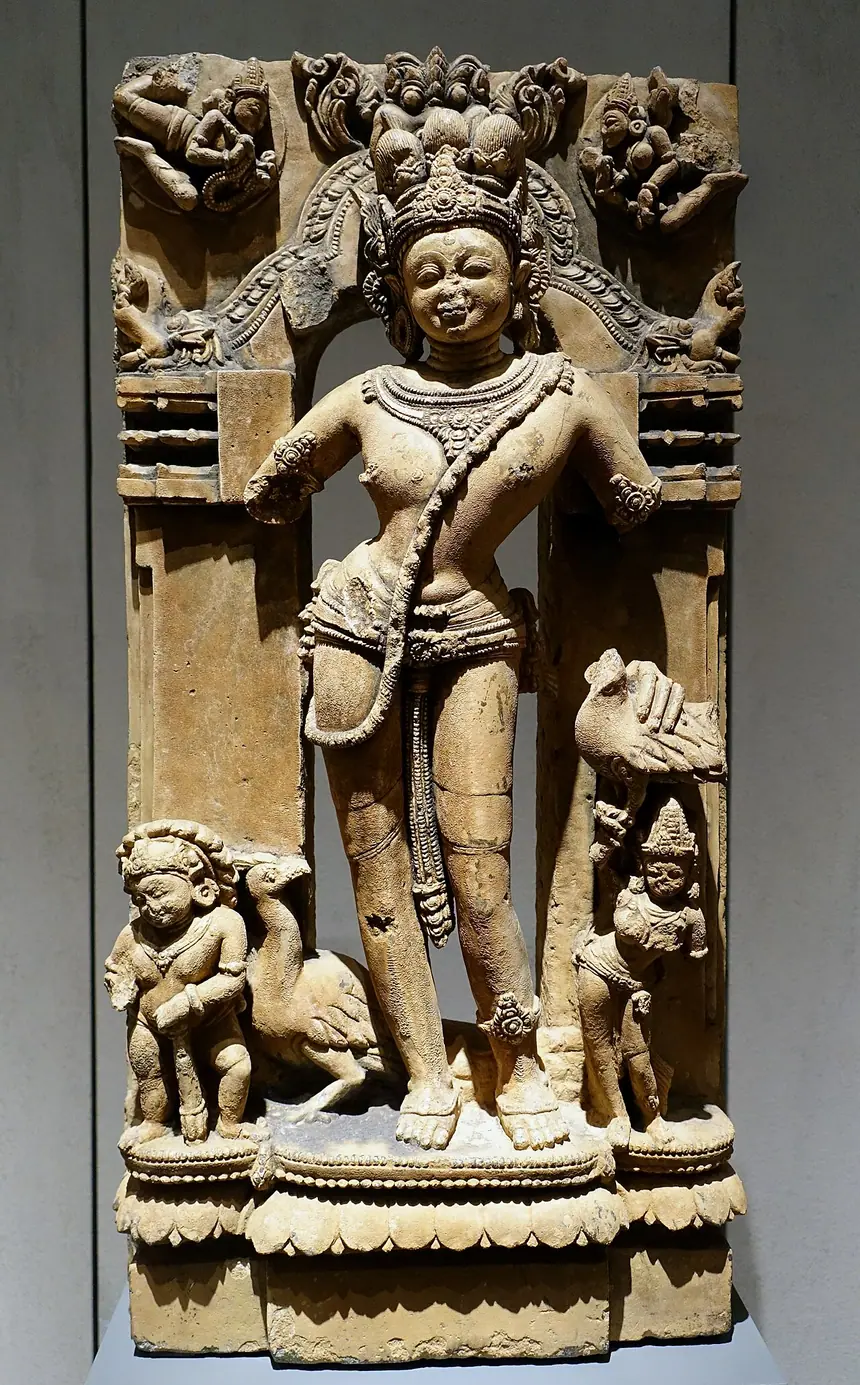 Thần Skanda (Karttikeya) đứng cạnh chim công. Đá phiến, Odisha, thế kỷ 13. Bảo tàng Dân tộc học Berlin.
