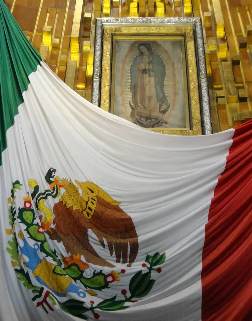 Tấm áo choàng (tilma) mang hình Đức Mẹ Guadalupe, lồng trong khung phía trên quốc kỳ Mexico. Vương cung thánh đường Đức Mẹ Guadalupe, thành phố Mexico. Ảnh chụp năm 2013.