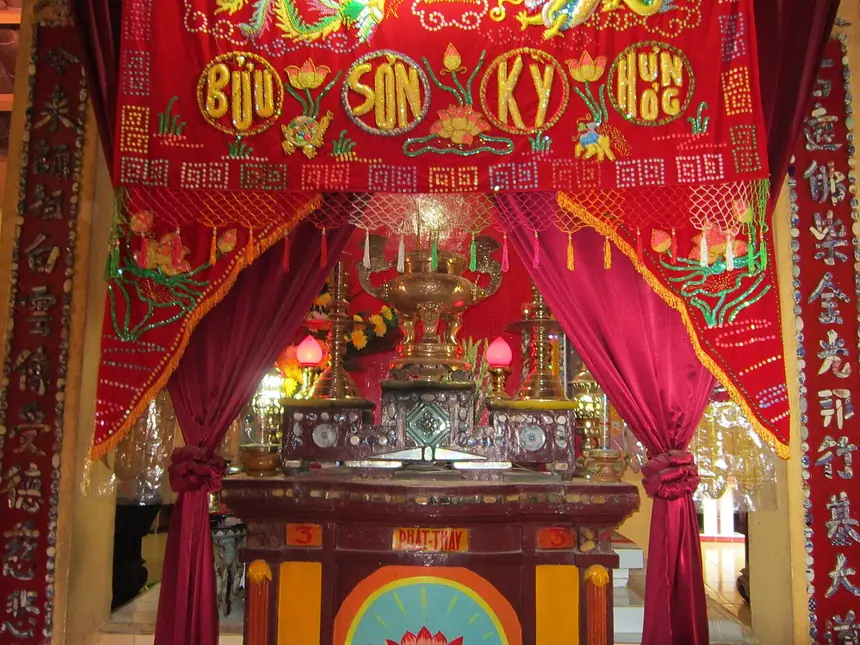 Bàn thờ Đức Phật Thầy Tây An trong hậu điện chùa Thới Sơn, An Giang. Phía trên là bức màn thêu bốn chữ Bửu Sơn Kỳ Hương, phía trong là tấm trần điều đỏ. Ảnh chụp năm 2013.