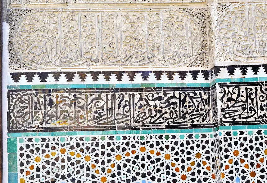 Tường trường Bou Inania, Fes, Maroc: gạch men ghép hình học (zellij) ở dưới, dải chữ Ả Rập và thạch cao chạm ở trên.