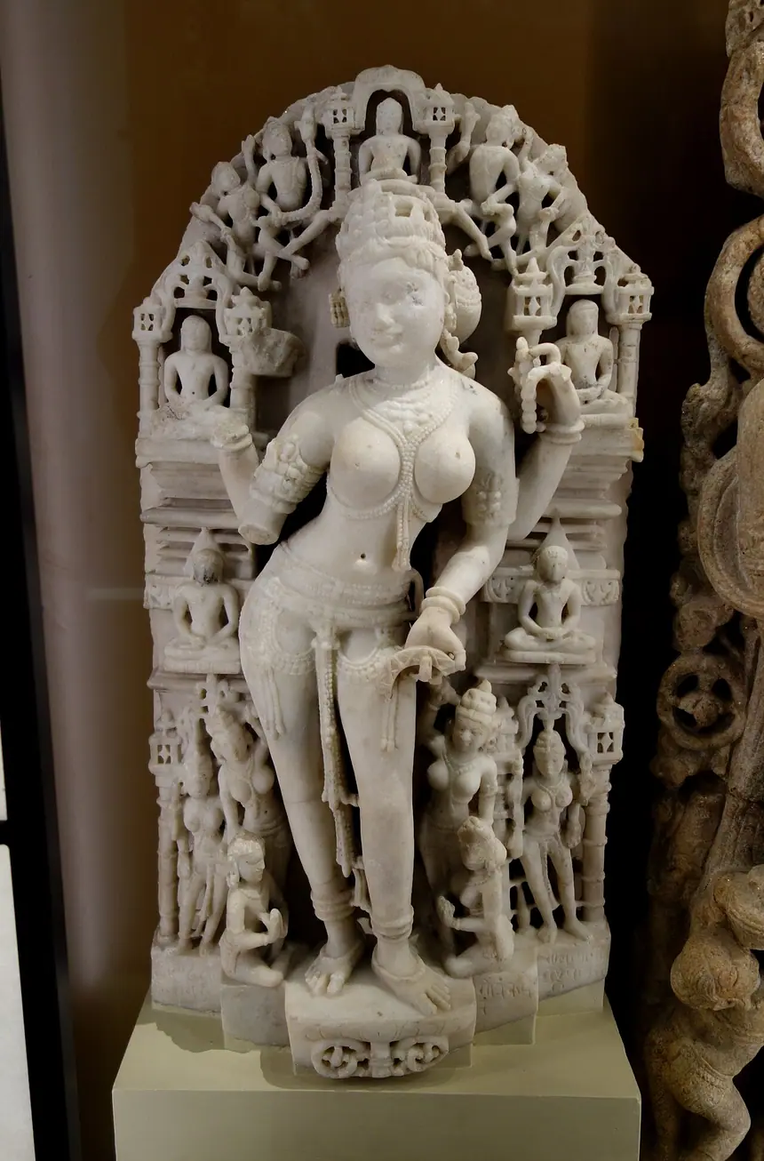 Sarasvati, nữ thần của tri thức, quanh là các vị Tirthankara nhỏ, chư thiên và người cúng. Cẩm thạch, Rajasthan, khoảng năm 1050 tới 1100. Bảo tàng Anh, London.