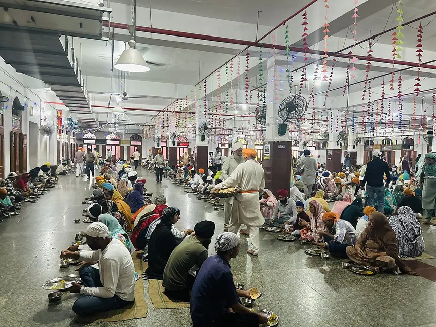 Nhà ăn langar ở Đền Vàng, Amritsar: mọi người ngồi thành hàng trên sàn, người phục vụ đi dọc các hàng. Ảnh chụp năm 2024.
