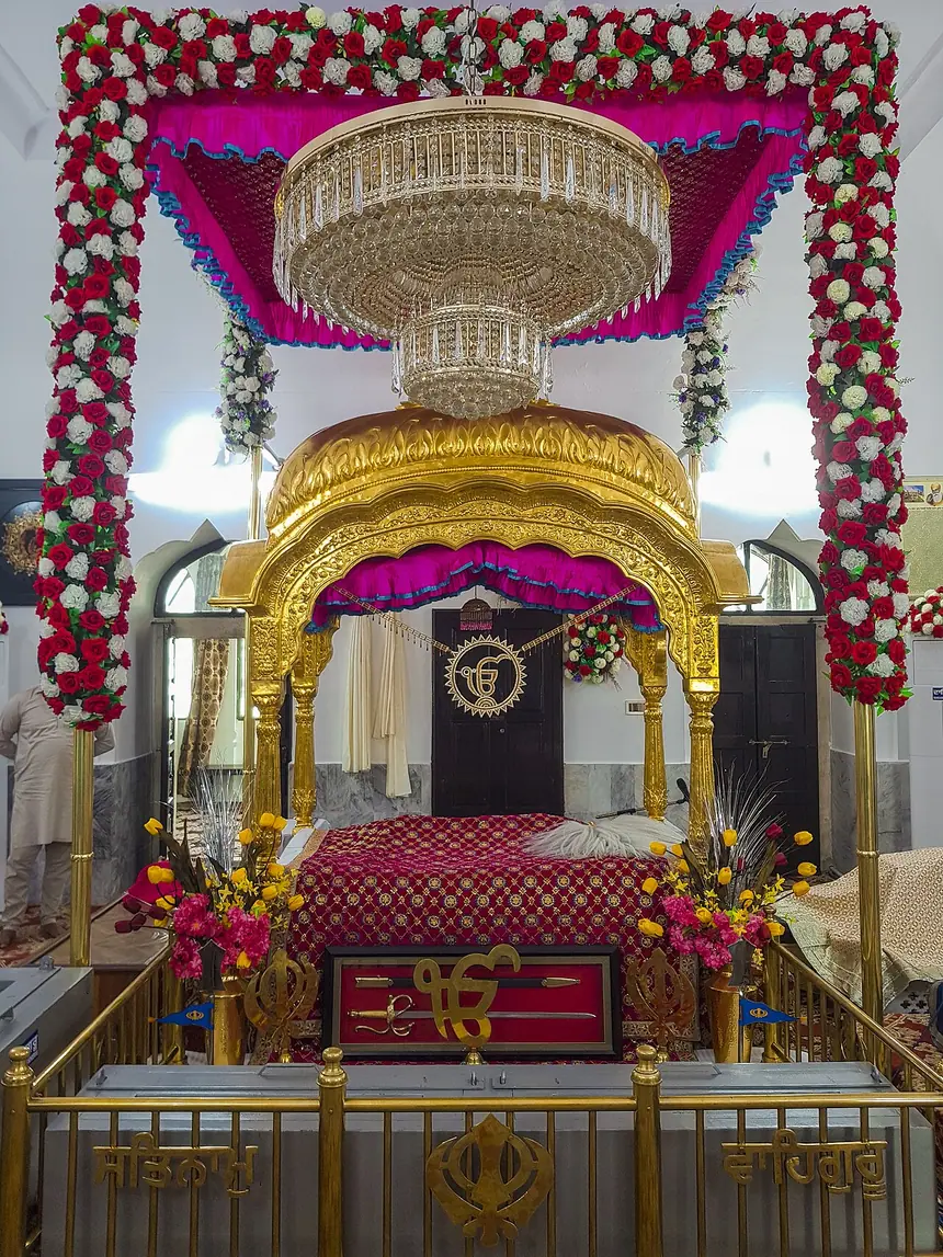 Palki trong Gurdwara Darbar Sahib, Kartarpur, Pakistan: mái vòm vàng, tán vải phía trên, chỗ đặt Kinh phủ khăn rumala. Lan can phía trước mang hình Khanda, vách sau mang chữ Ik Onkar. Ảnh chụp năm 2021.