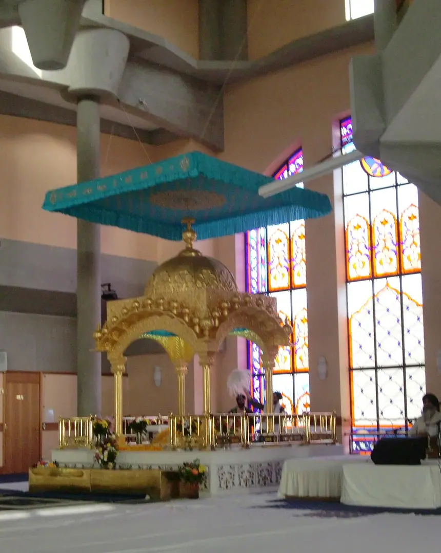 Chỗ tôn trí Guru Granth Sahib trong gian chính: kiệu palki mạ vàng đặt trên bục, phía trên căng tấm tán chanani màu lam. Gurdwara Sri Guru Singh Sabha, Southall, London. Ảnh chụp năm 2011, được gurdwara cho phép.