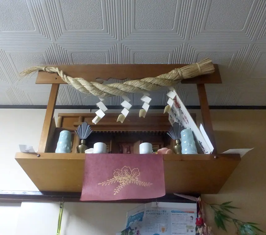 Một kệ thờ thần (kamidana) trong nhà ở vùng Tokyo: ngôi đền gỗ nhỏ đặt sát trần, phía trên giăng dây shimenawa. Ảnh năm 2017.