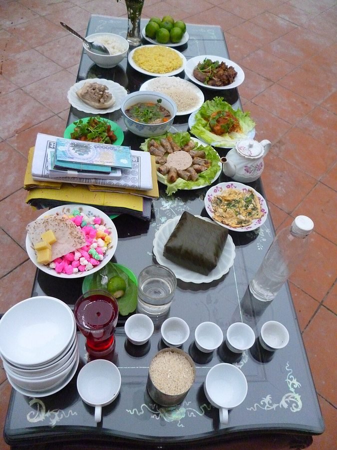 Traditional Year-End Reunion (Tat Nien) offering meal. Savory year-end ancestral feast featuring peeled square sticky-rice cake (banh chung), fried spring rolls, pork roll, steamed sticky rice, hot soup, betel-areca and five ceremonial wine cups.