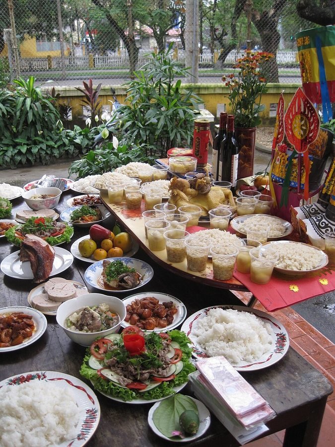 Traditional Tet offering table in Hue, Central Vietnam. Household Lunar New Year offering table in Hue arranged with whole boiled chicken, steamed sticky rice, sweet soup bowls, savory dishes, betel leaf, fresh flowers and ceremonial deity caps.