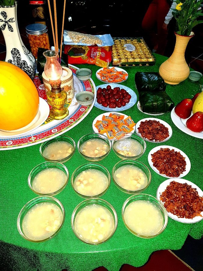 Red gac sticky rice, lotus-seed mung-bean sweet soup and banh chung. Auspicious sweet offering tray with crimson gac sticky rice, whipped mung-bean sweet soup topped with lotus seeds, a pair of green banh chung cakes, oil lamp and yellow chrysanthemums.